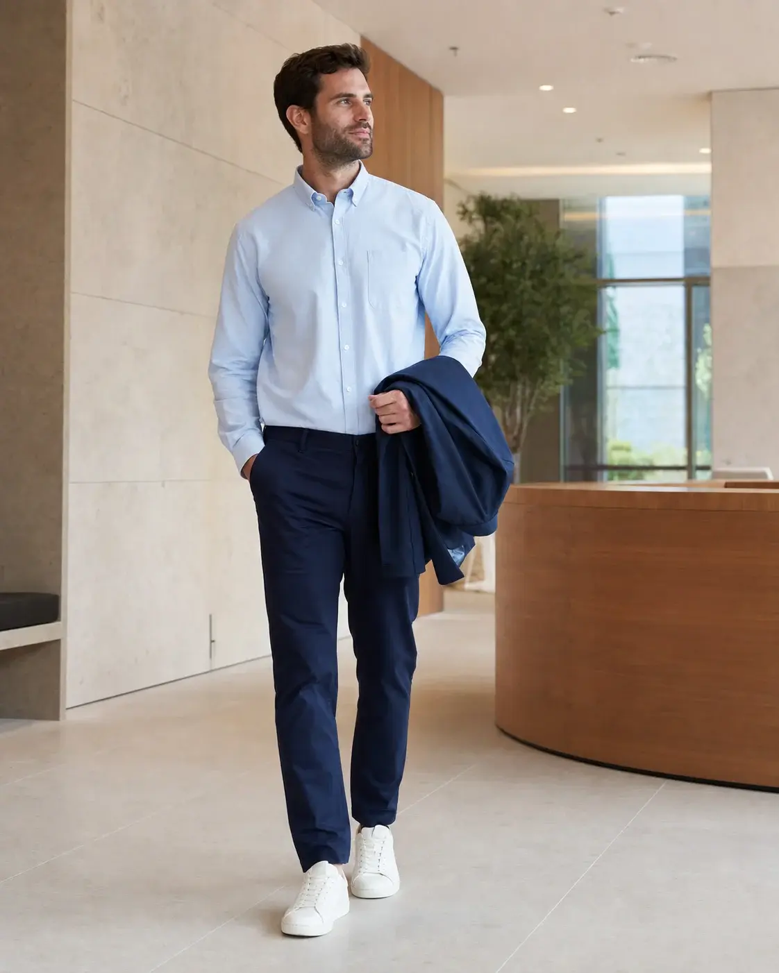 Hombre con camisa azul, chino marino y zapatillas blancas en una oficina contemporánea.